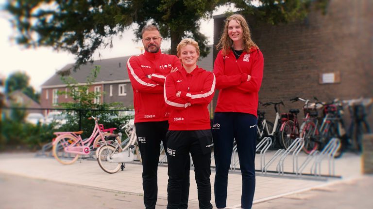 Drie buurtsportcoaches van Rucphen Beweegt in rode trainingsjassen bij een basisschool